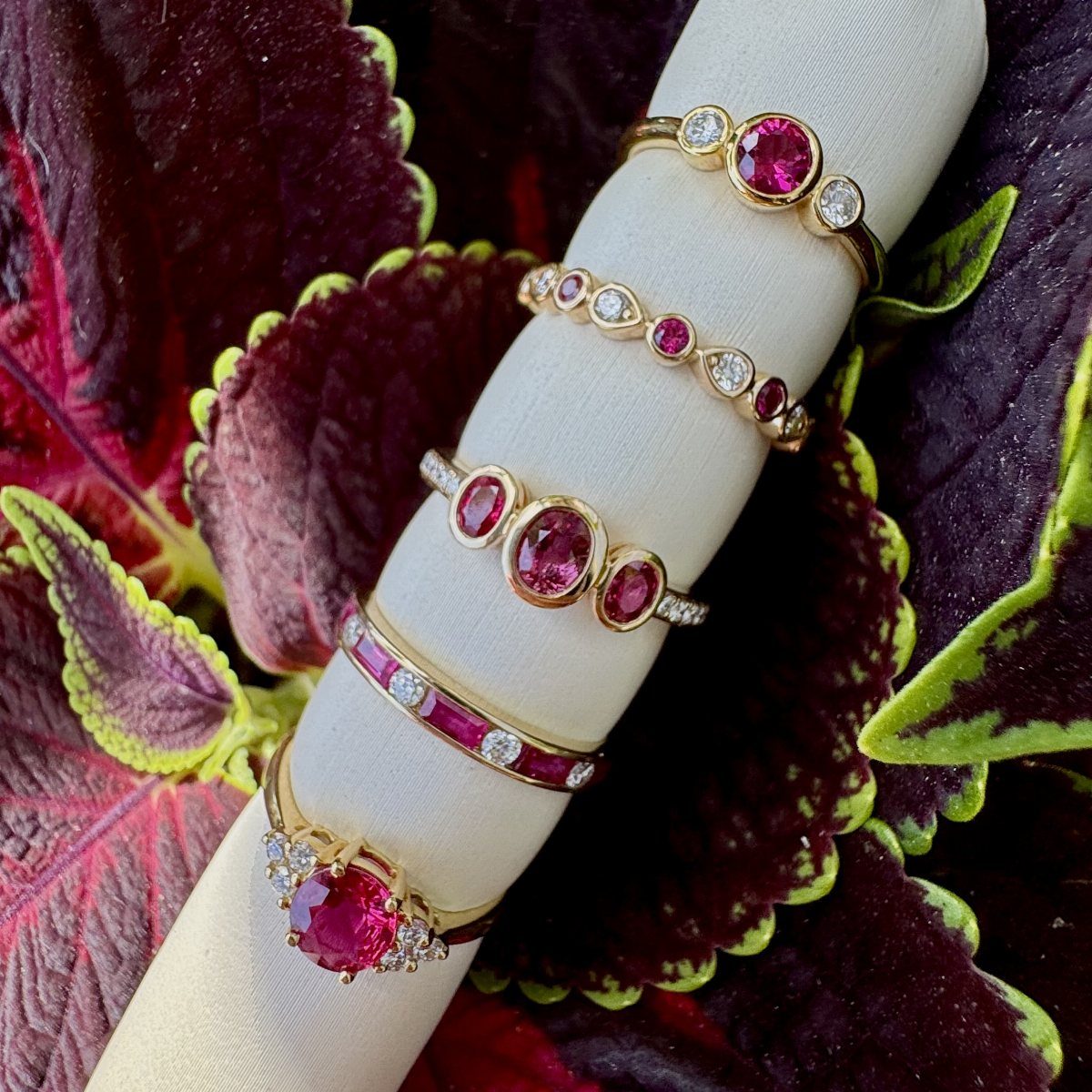 Gold rings with red rubies and diamonds on a white stand among red leaves