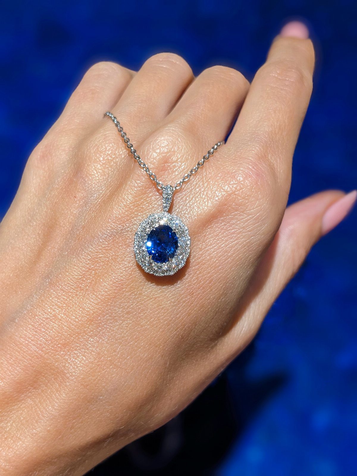 Silver necklace with a blue sapphire pendant resting on a person's hand.