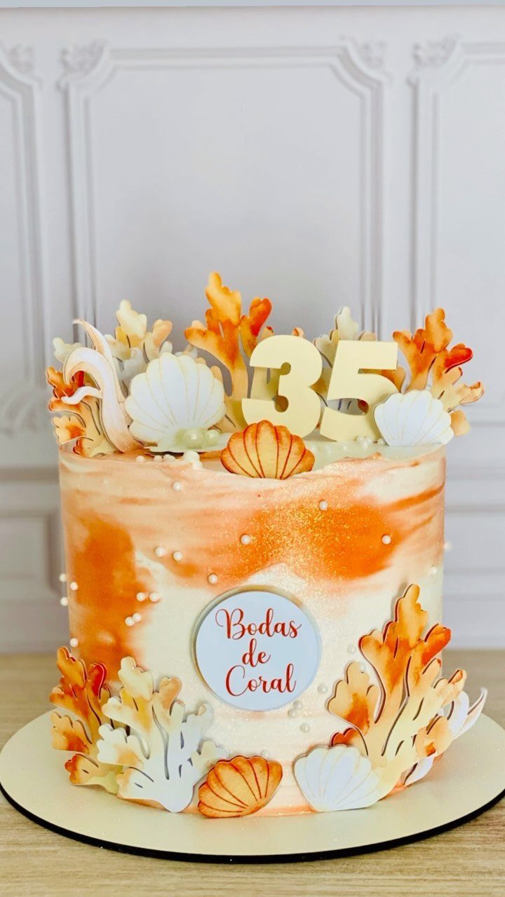 Anniversary cake with orange frosting, coral decorations, seashells, and a gold 35 topper.