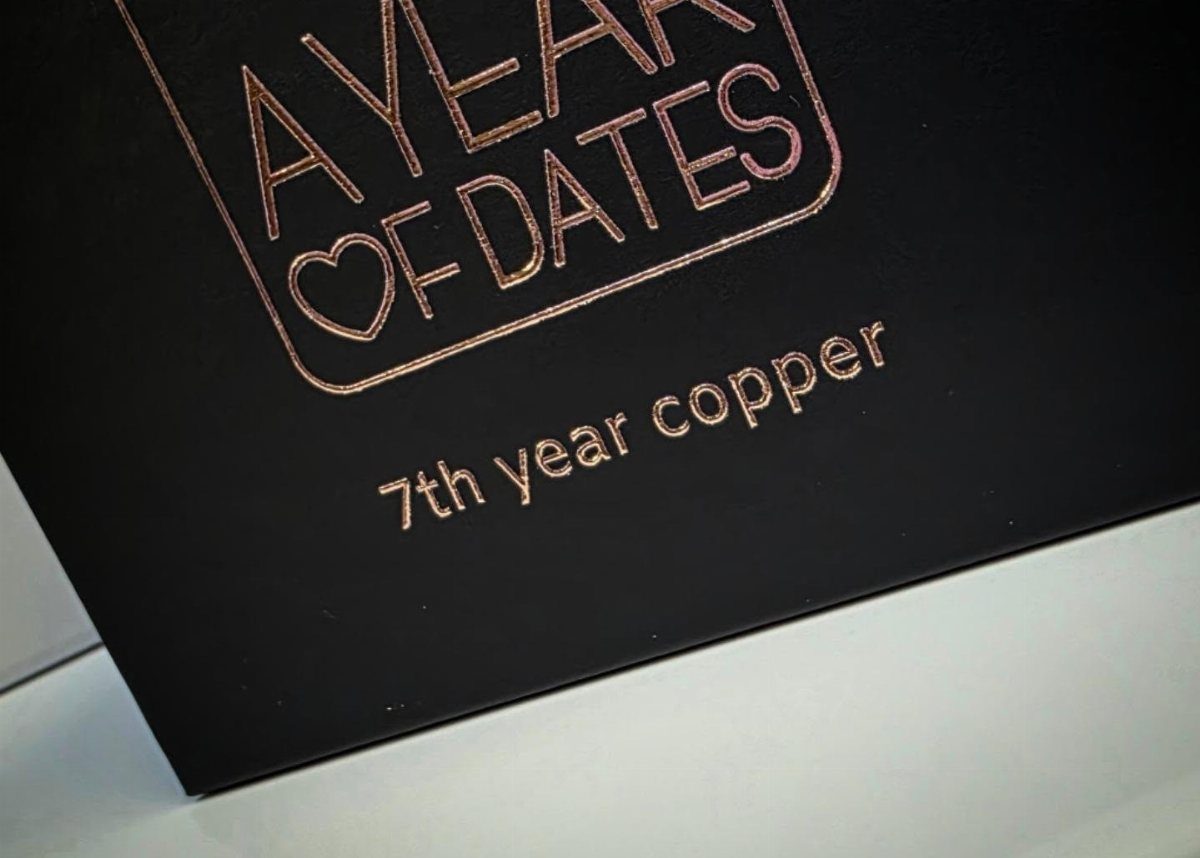 Black card with copper foil text reading A Year of Dates 7th year copper