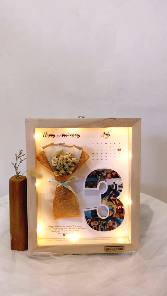 Illuminated wooden shadow box with dried flowers, photos, and anniversary greeting text.