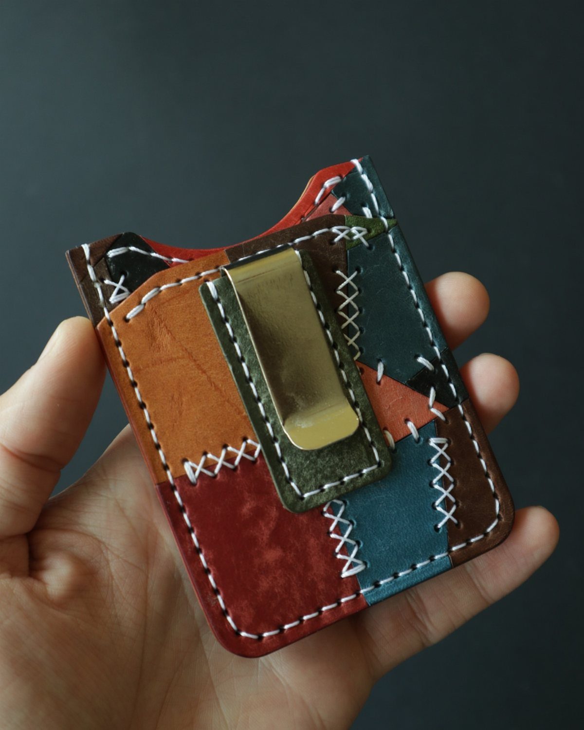 Handmade multicolored leather patchwork wallet with white stitching and a metal clip.