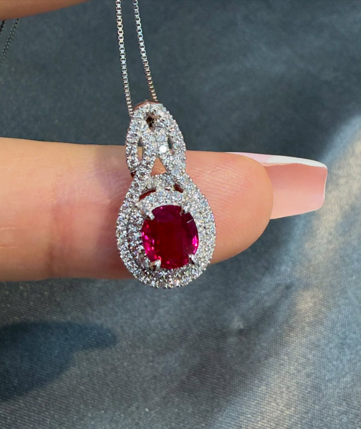 Ruby gemstone necklace with diamond accents held against a grey background.