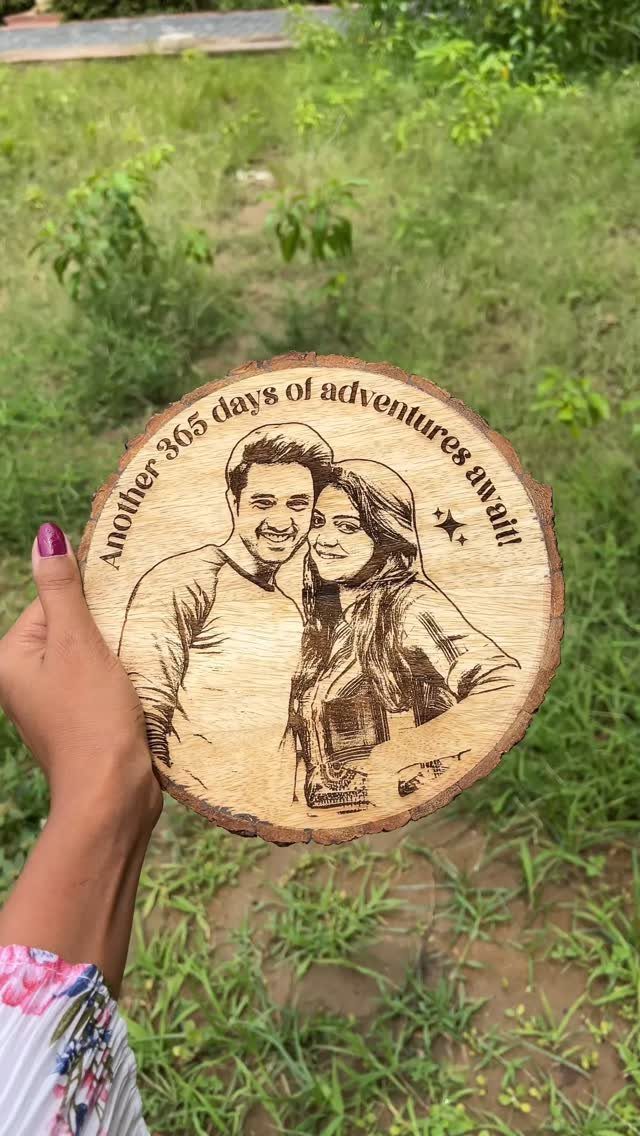 Engraved wooden slice showing a couple's portrait with an anniversary message held outdoors.