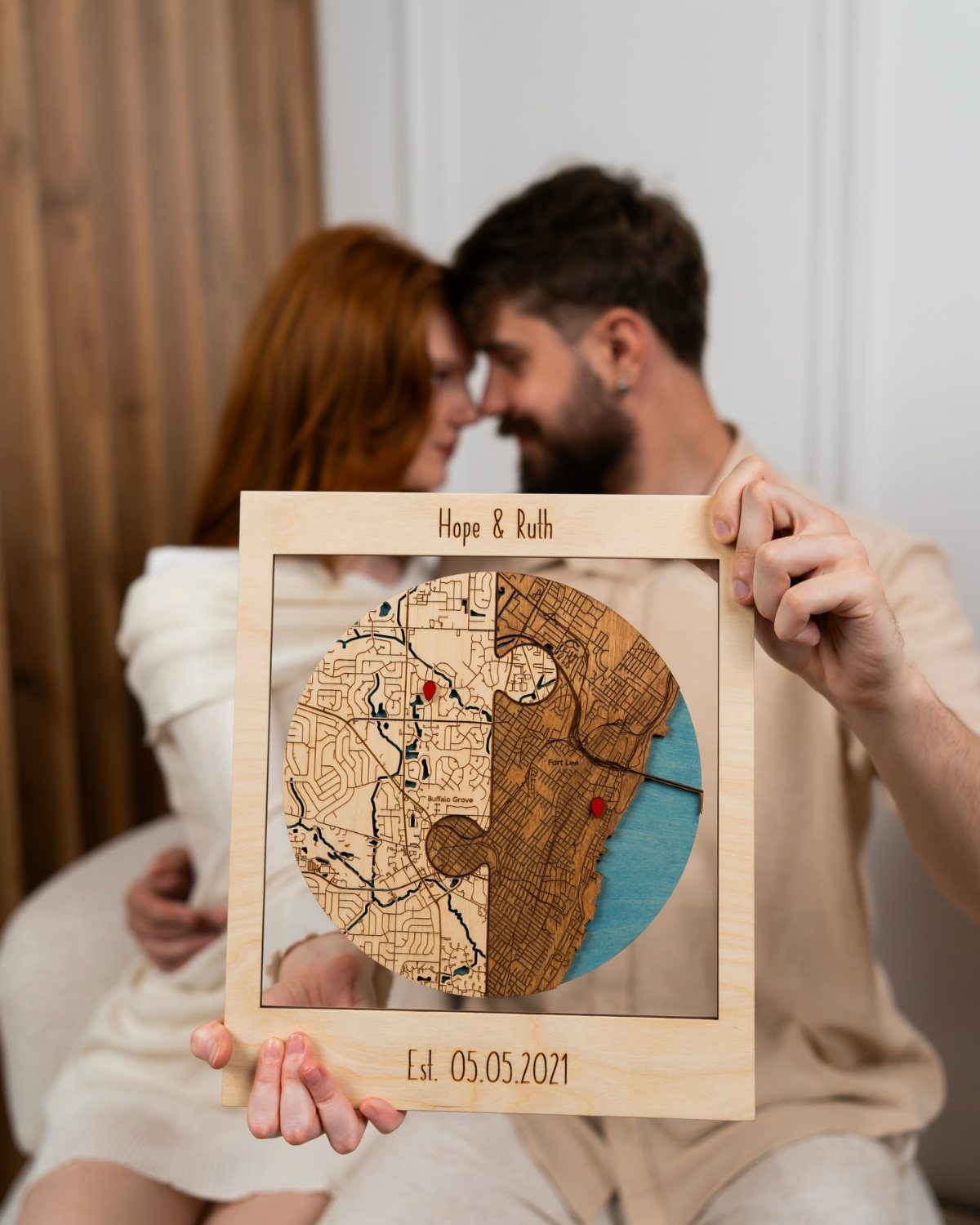 Couple holding a circular engraved wooden map framed with personalized names and date.