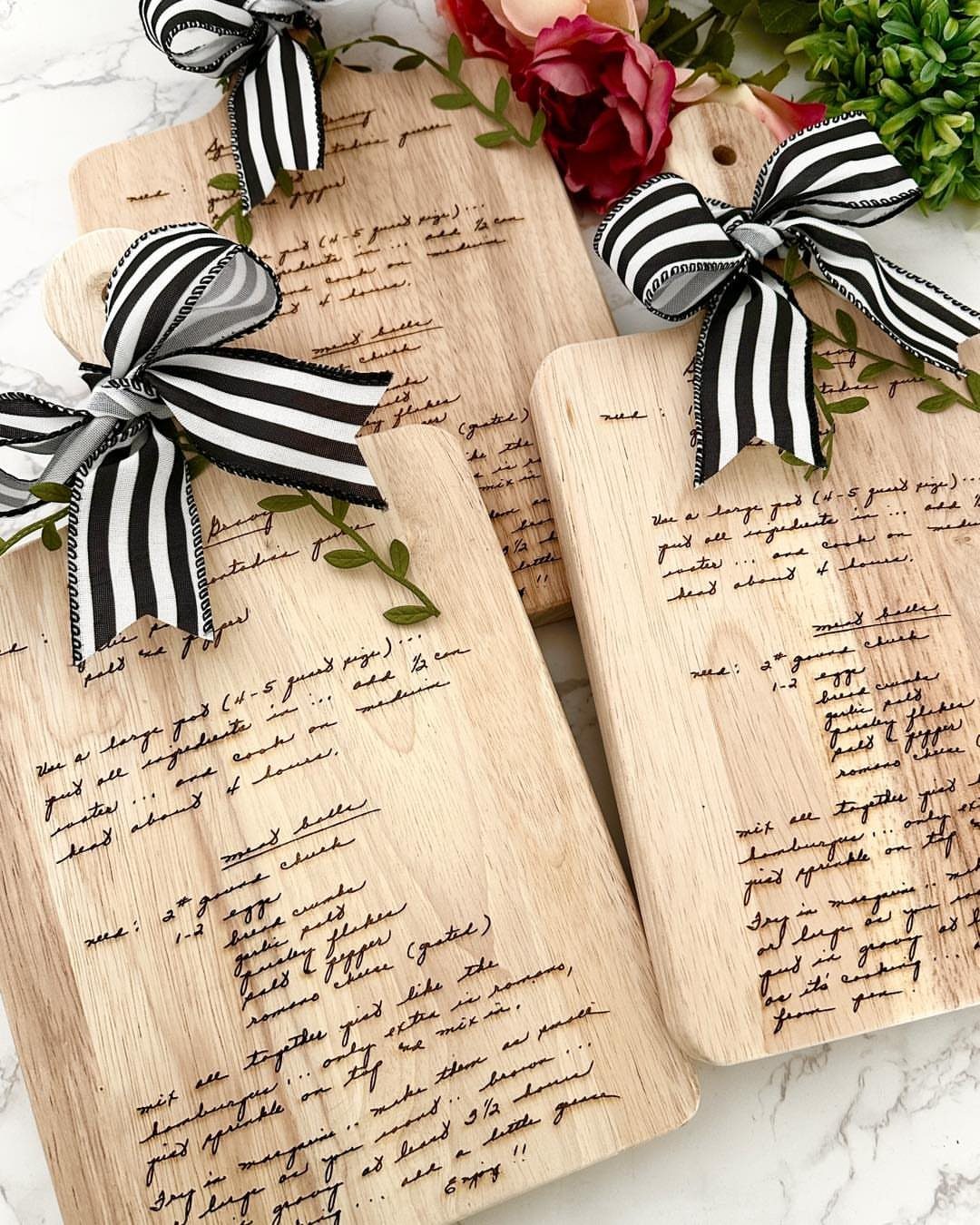 Wooden cutting boards with engraved handwriting and black and white striped bows.