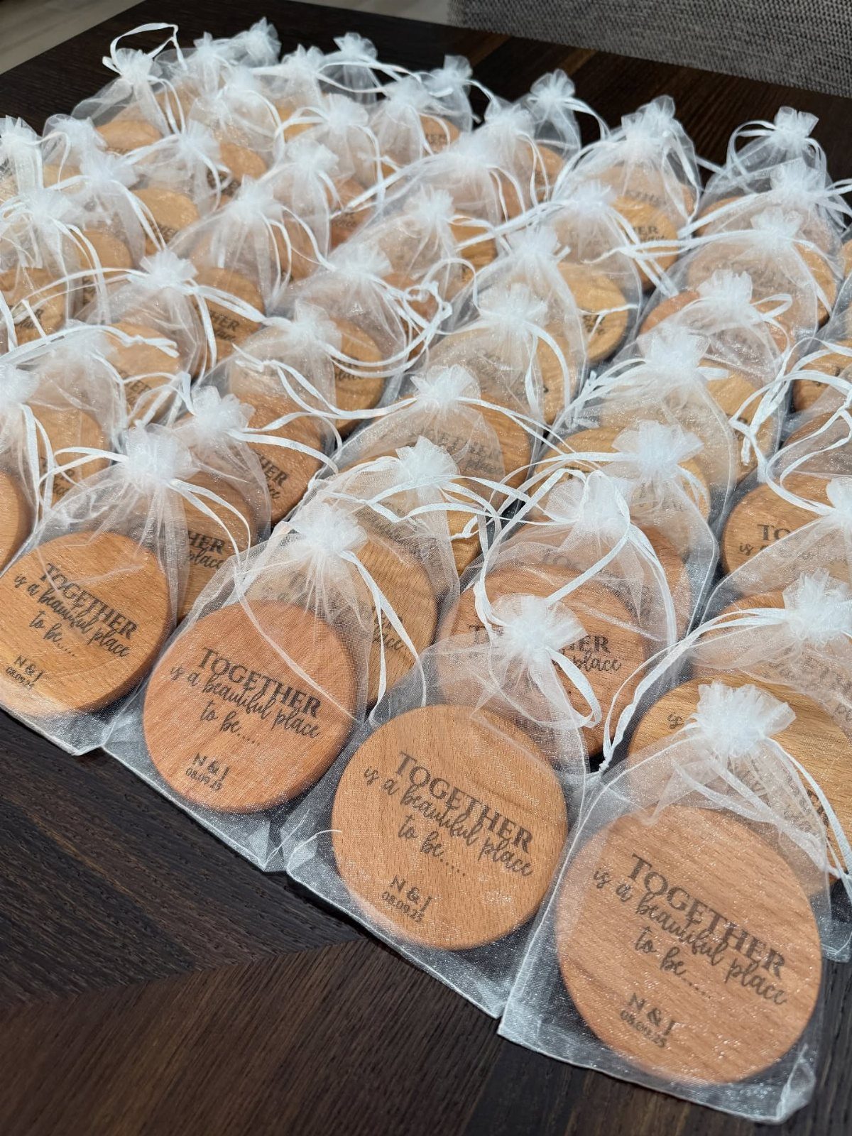Round engraved wooden coasters wrapped in white organza bags on a dark table