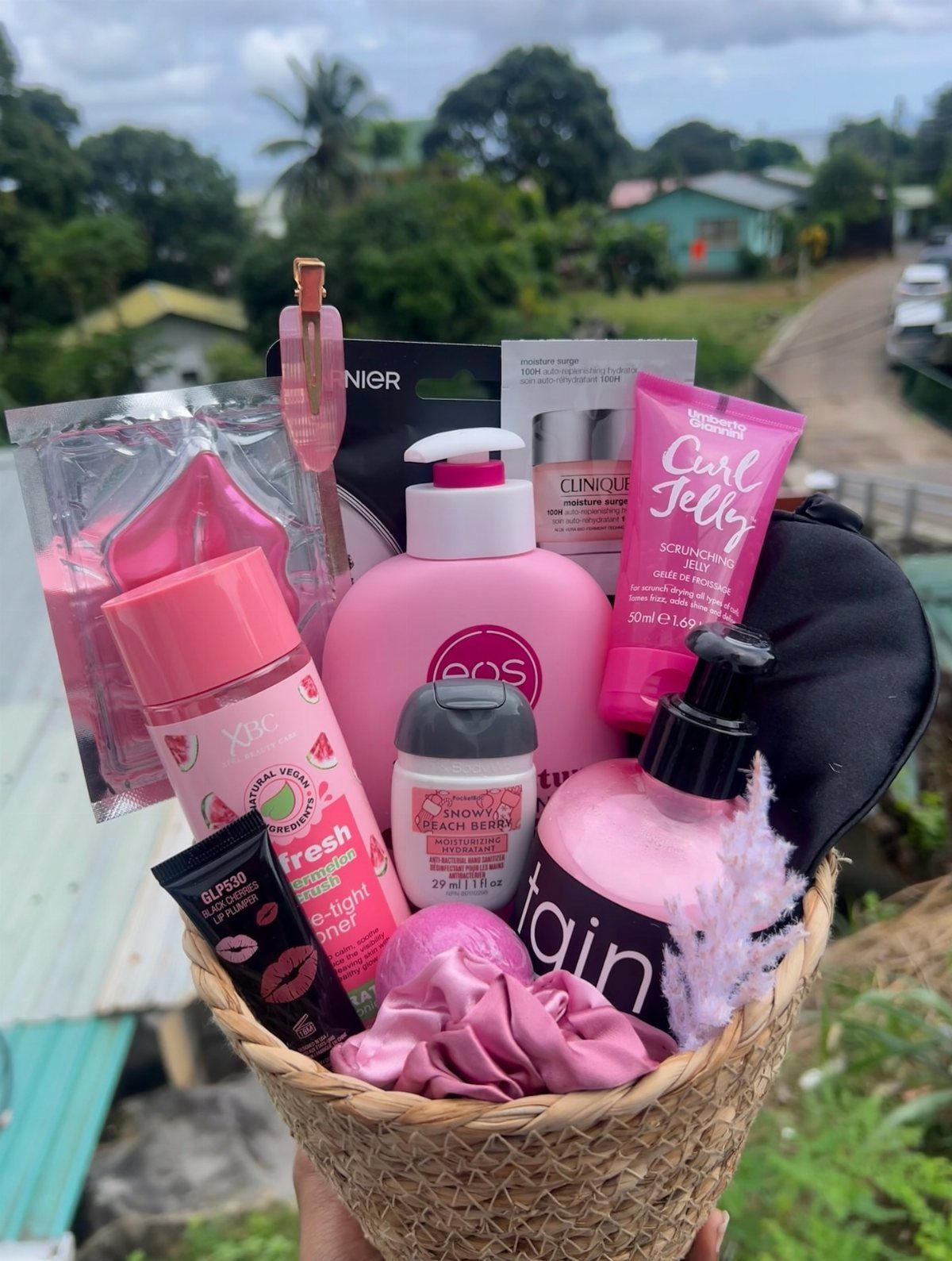 Woven basket filled with pink skincare products, lotions, and a sleep mask outdoors.