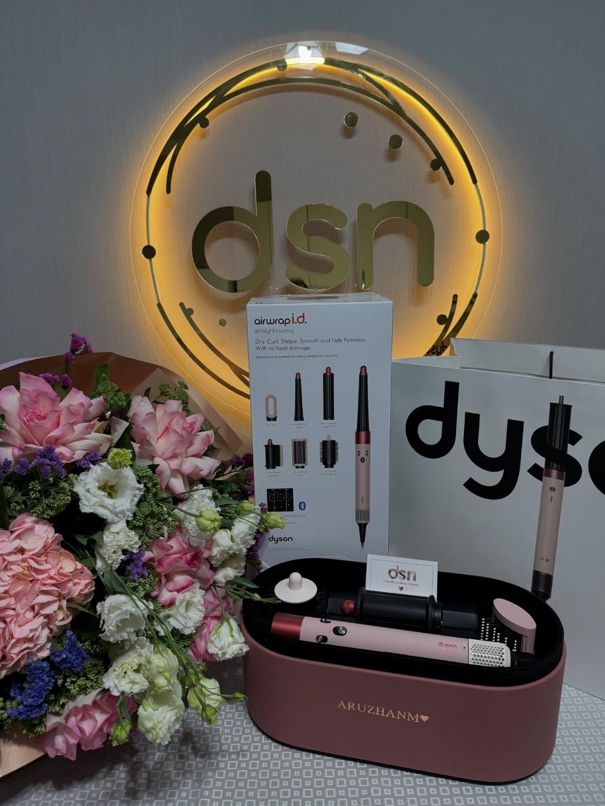 Dyson Airwrap hair styler with packaging and a bouquet of pink flowers.