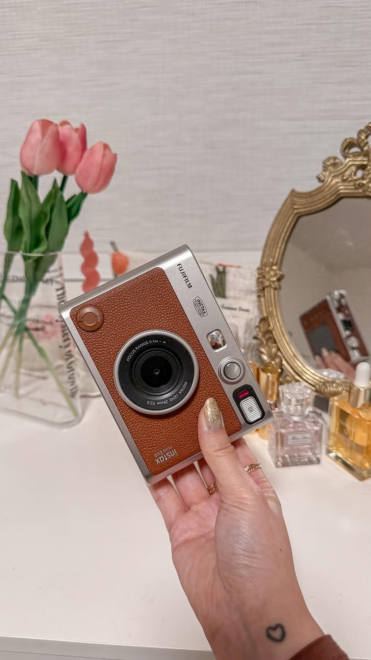 Fujifilm Instax Mini 40 instant camera held in a hand near pink tulips.