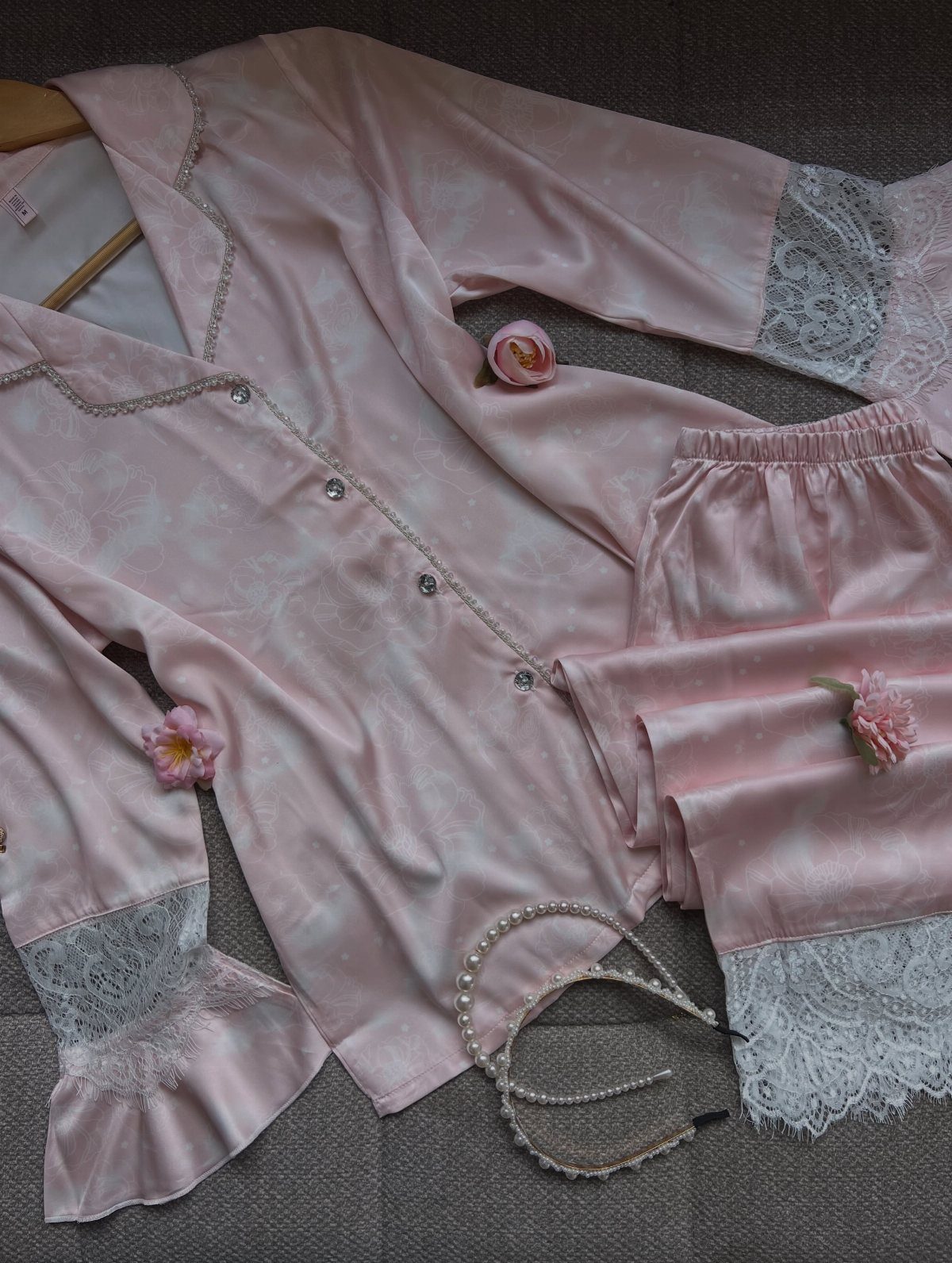 Pink satin pajama set with lace trim, decorated with rosebuds and a pearl necklace.