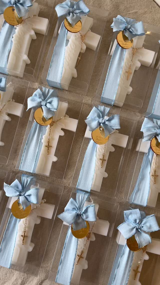 White cross-shaped favors with light blue ribbons and gold cross charms in boxes.
