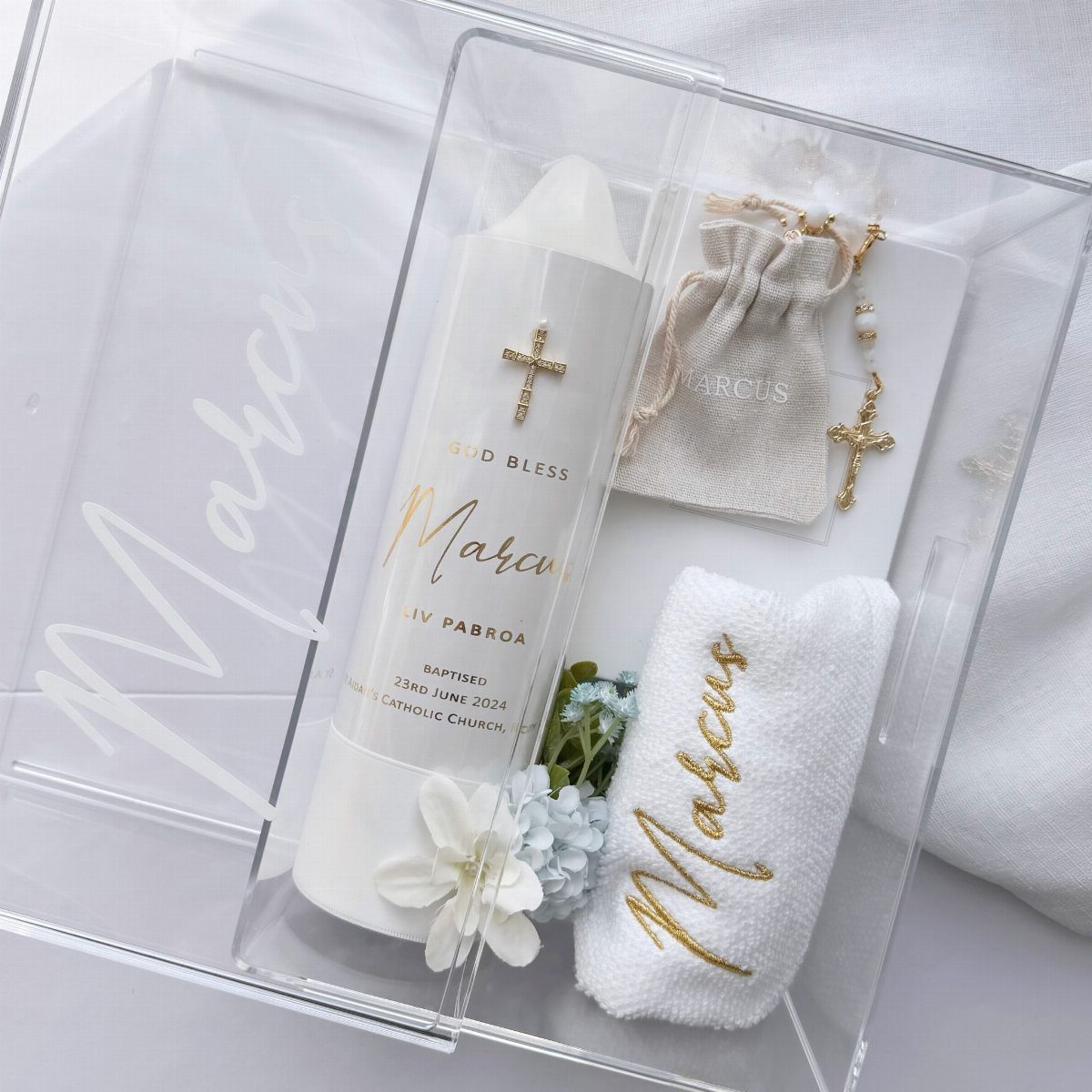 Baptismal gift set with personalized candle, rosary, and embroidered cloth in acrylic box.
