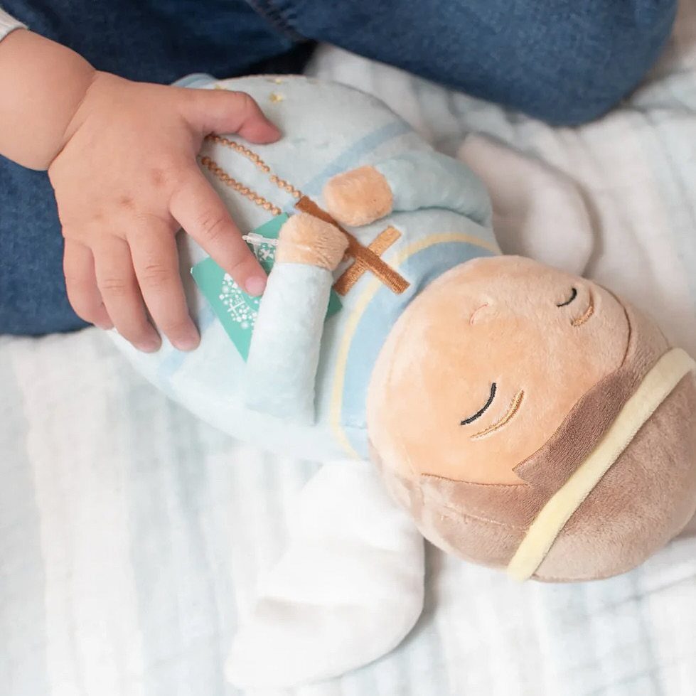Baby's hand touching a plush guardian angel doll with blue robe and white wings