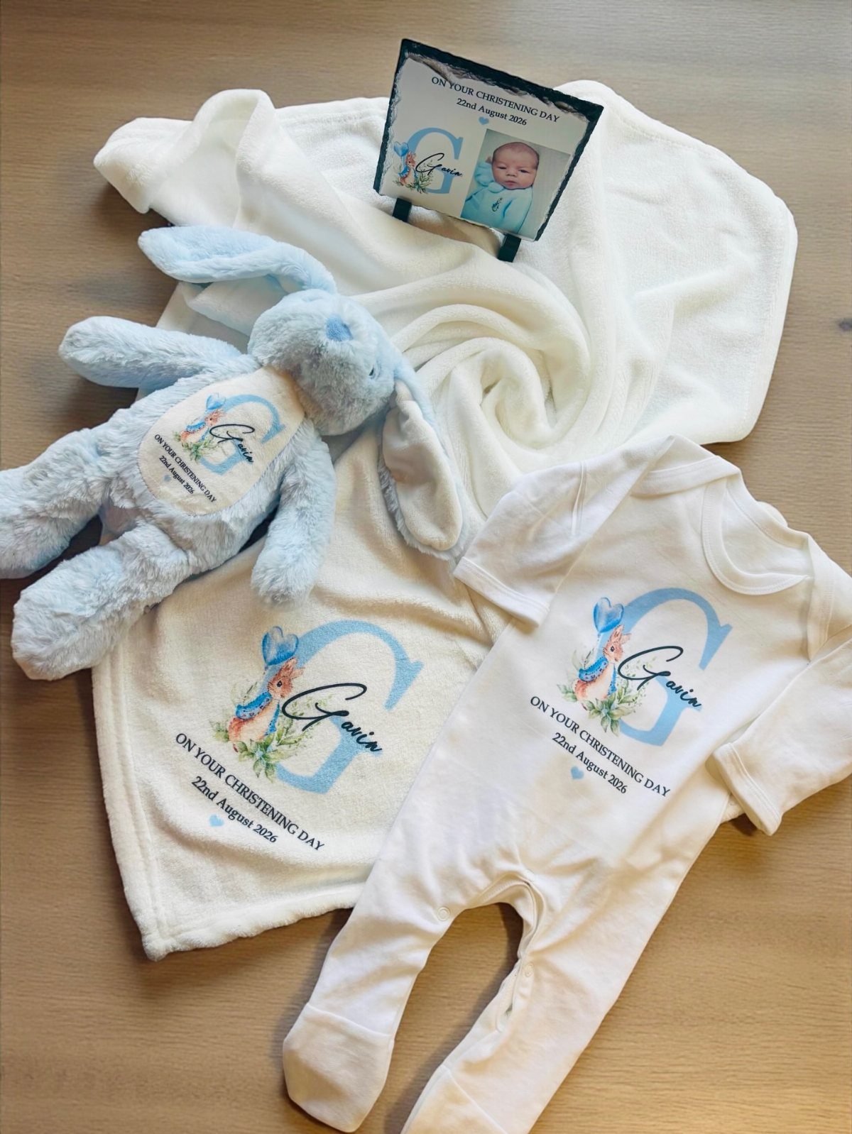 Personalized white baby blanket and bodysuit with blue embroidery and a plush bunny.