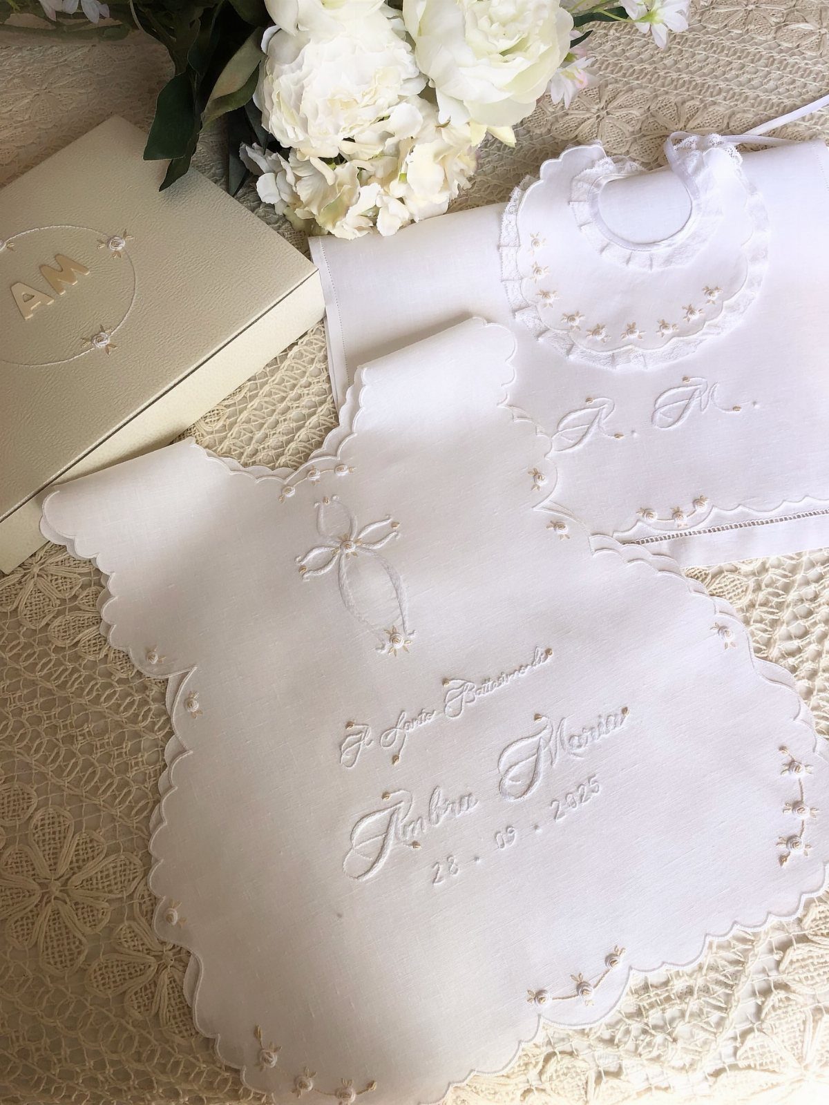 Embroidered white baby bibs with a cross and personalized text on lace.