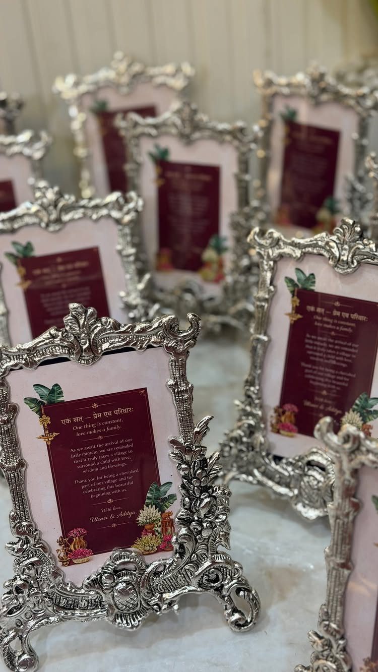 Ornate silver photo frames holding maroon invitation cards with gold text and flowers.