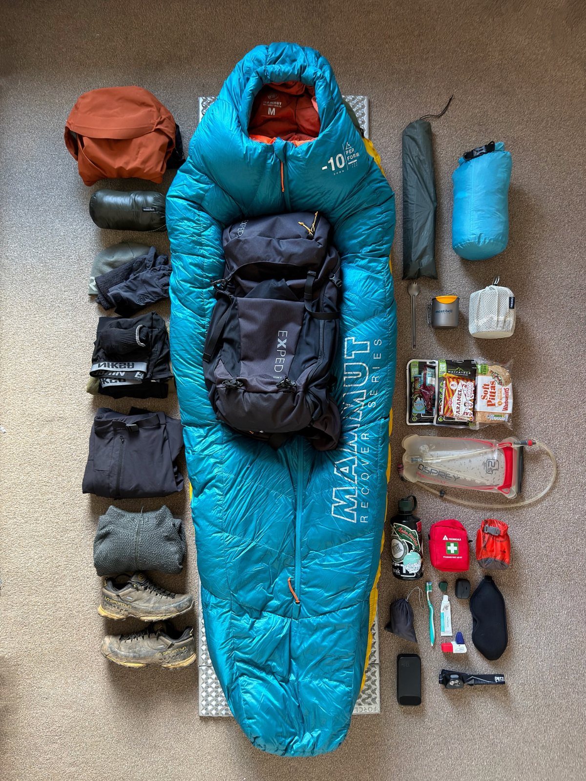 Camping gear including a blue sleeping bag, black backpack, and hiking boots laid out.
