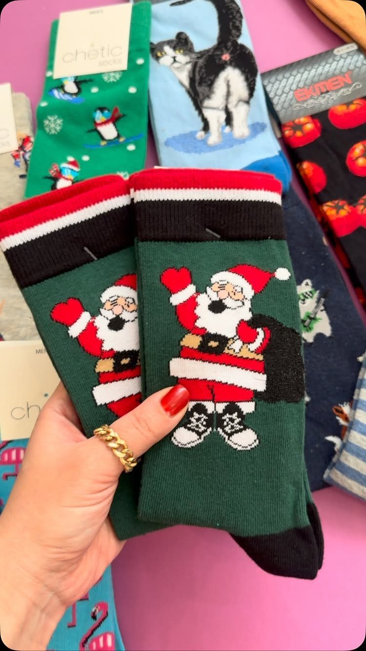 Green Santa Claus novelty socks held by a hand over other patterned socks.