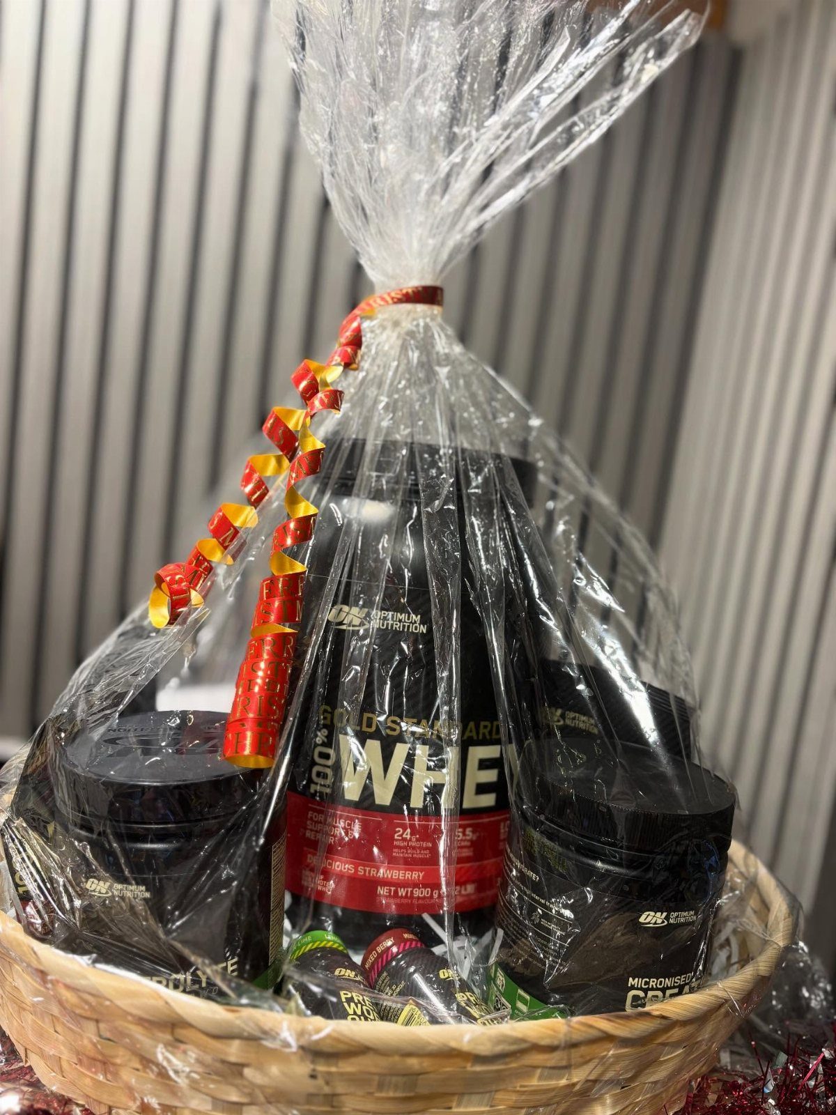 Wicker gift basket containing black tubs of whey protein powder wrapped in cellophane.