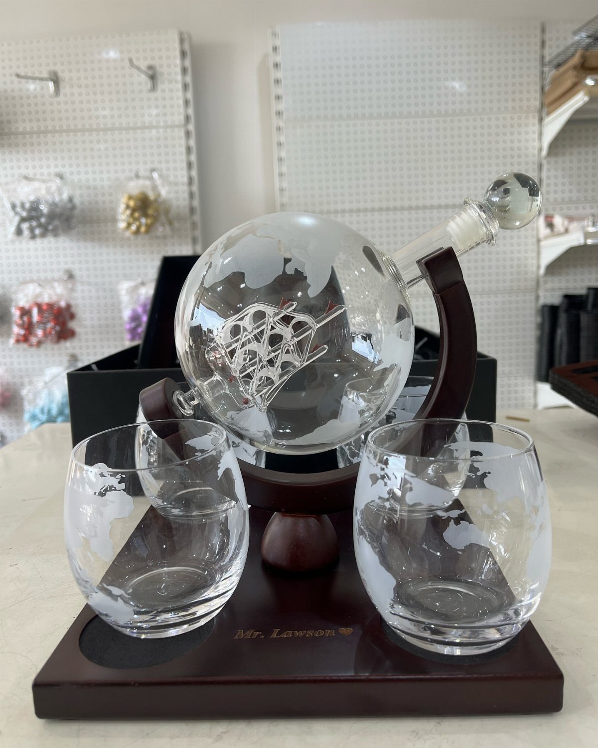 Globe-shaped glass decanter and two matching glasses on a dark wooden engraved stand.
