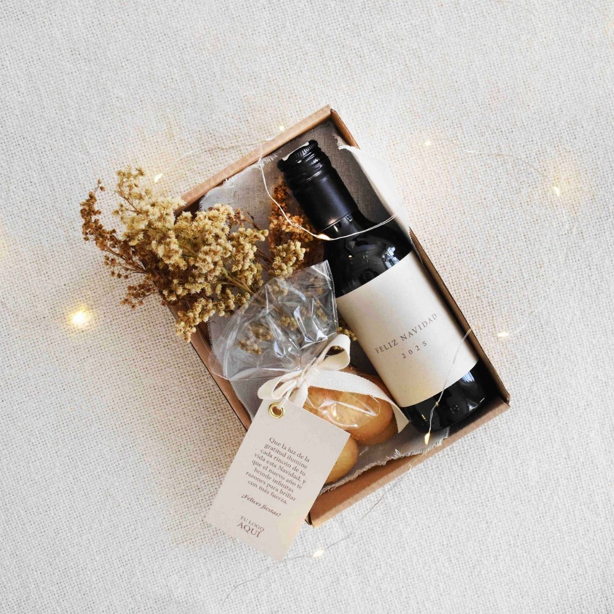 Christmas gift box with red wine, cookies, and dried flowers on white fabric