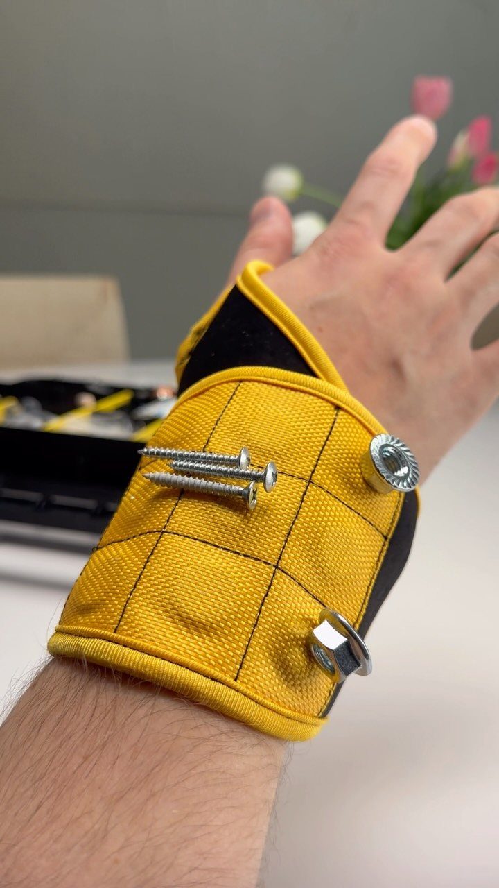 Yellow magnetic wristband holding silver screws and nuts on a person's wrist