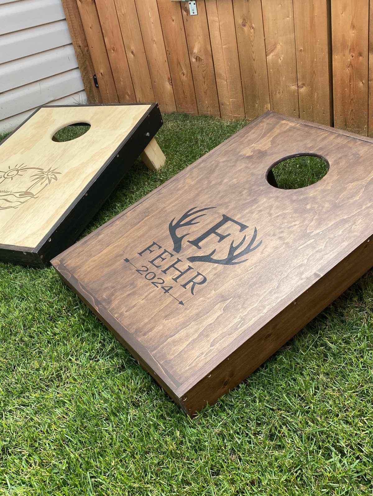 Two wooden cornhole boards on grass, one featuring a custom antler engraving.