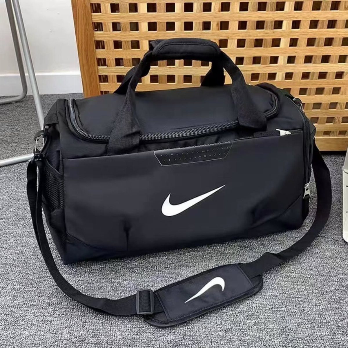 Black Nike duffel bag with white logo on a grey carpeted floor.