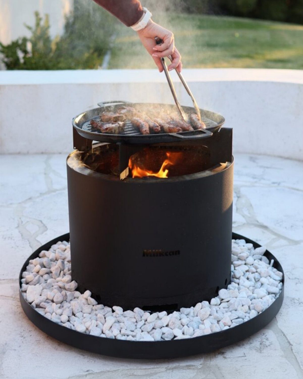 Black outdoor fire pit grill with meat cooking over flames on a patio