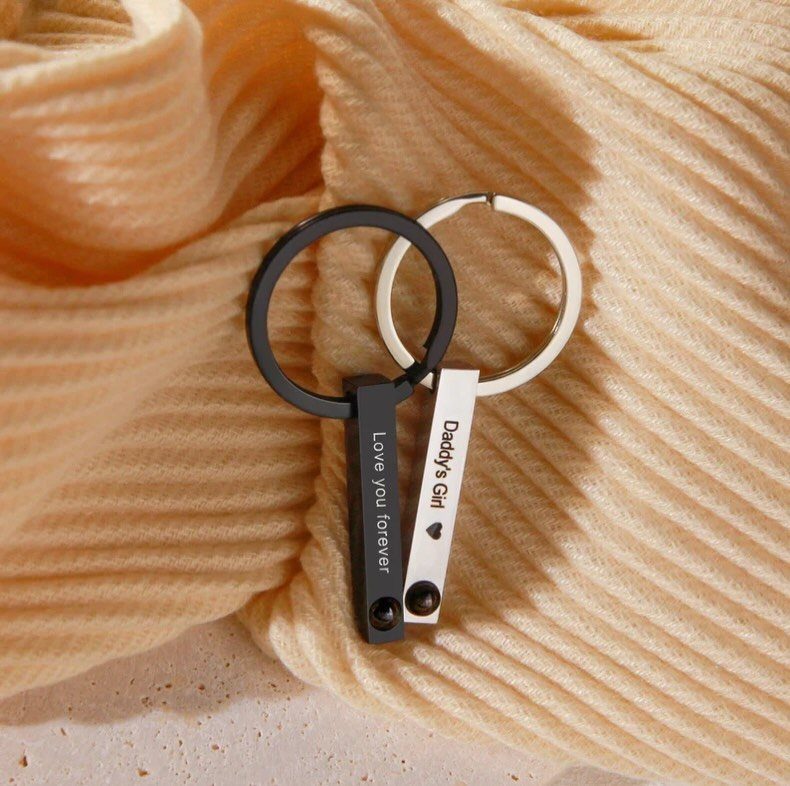 Two matching metal keychains with sentimental messages resting on yellow ribbed fabric.