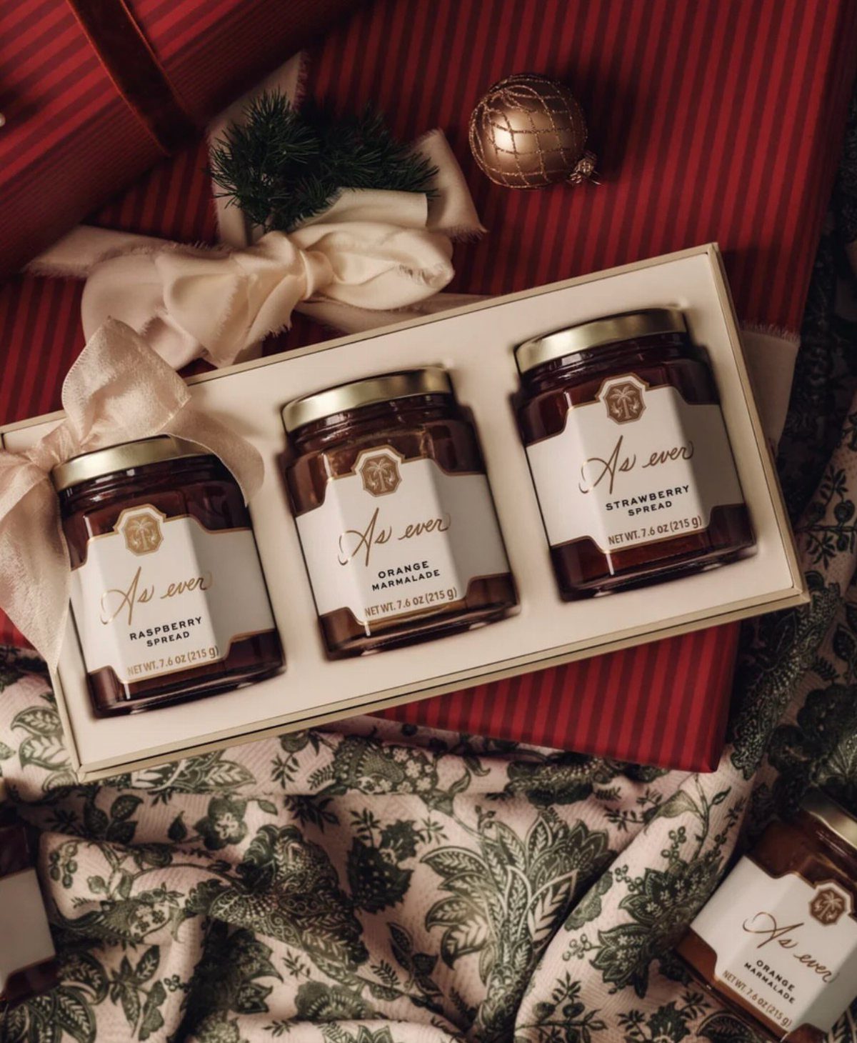 Three jars of fruit spreads in a white gift box on red striped background
