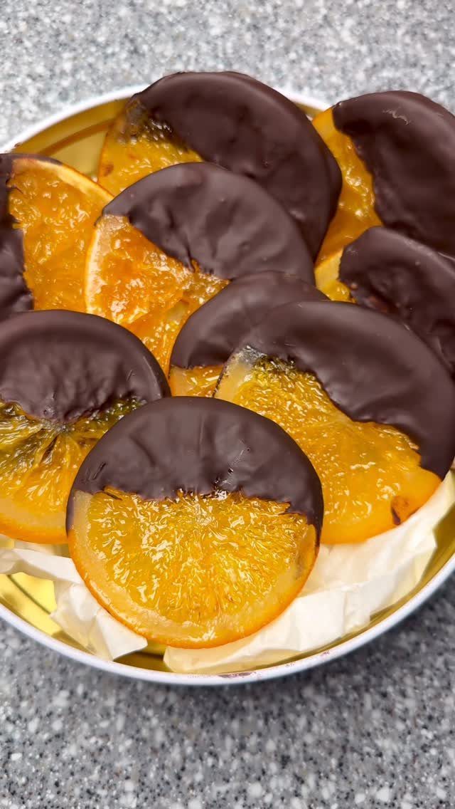 Chocolate dipped dried orange slices in a gold tin on a grey surface