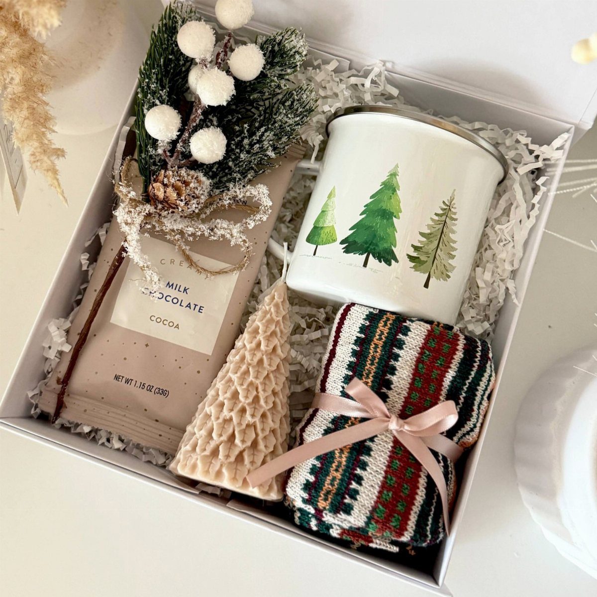 Christmas gift box containing chocolate, a pine tree mug, and knitted accessories.