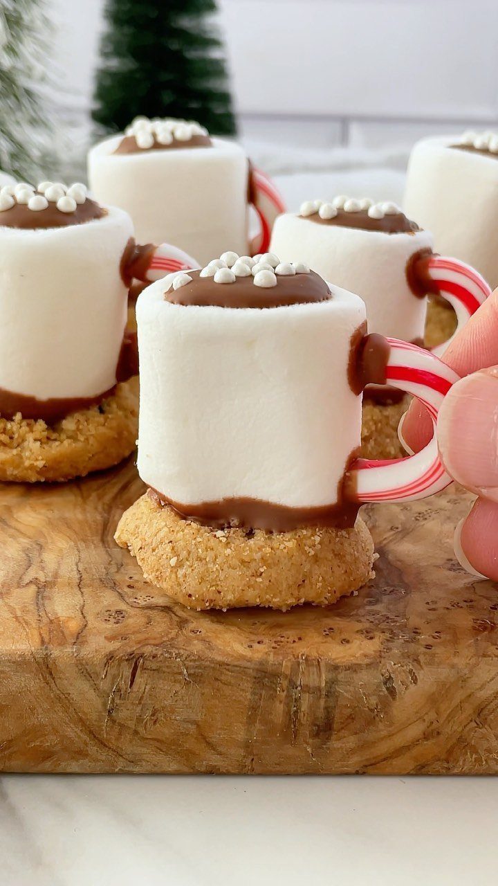 Marshmallow mug desserts with candy cane handles on a wooden serving board.