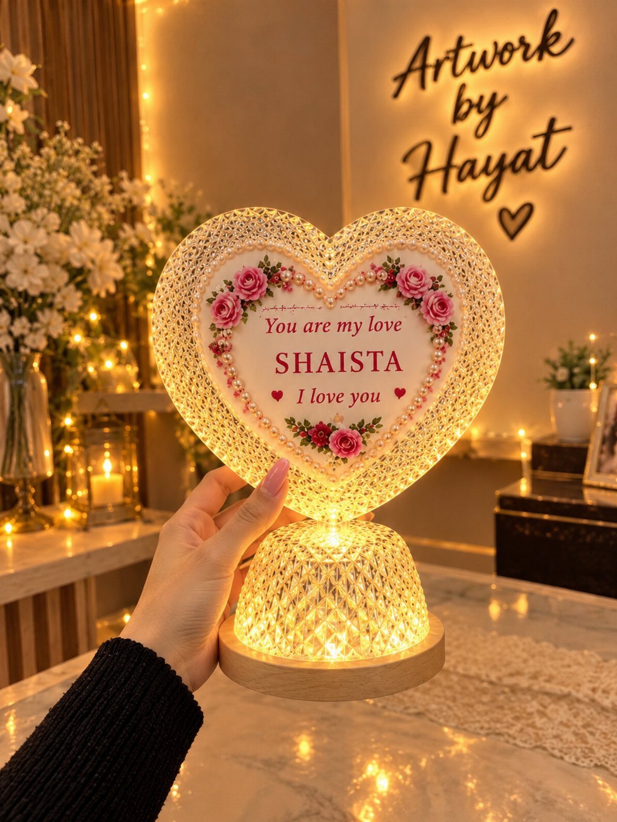 Heart-shaped illuminated lamp with personalized text and roses held by a hand.
