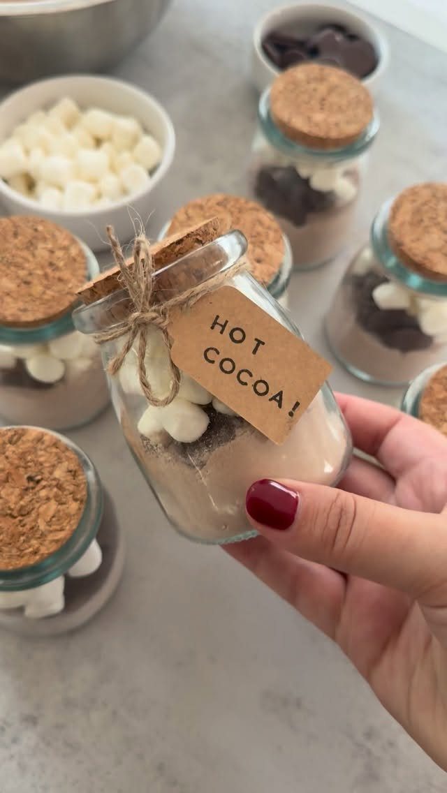 Hand holding a glass jar of hot cocoa mix with marshmallows and cork lid