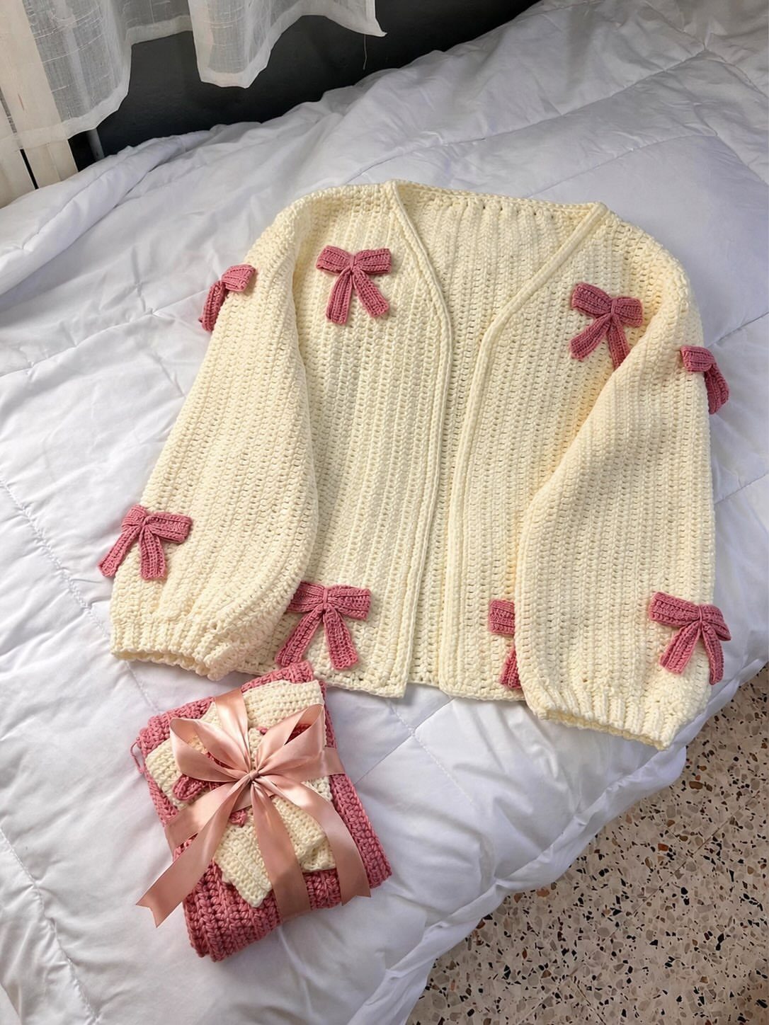 Cream knitted cardigan with pink bows and matching accessory on white bedding