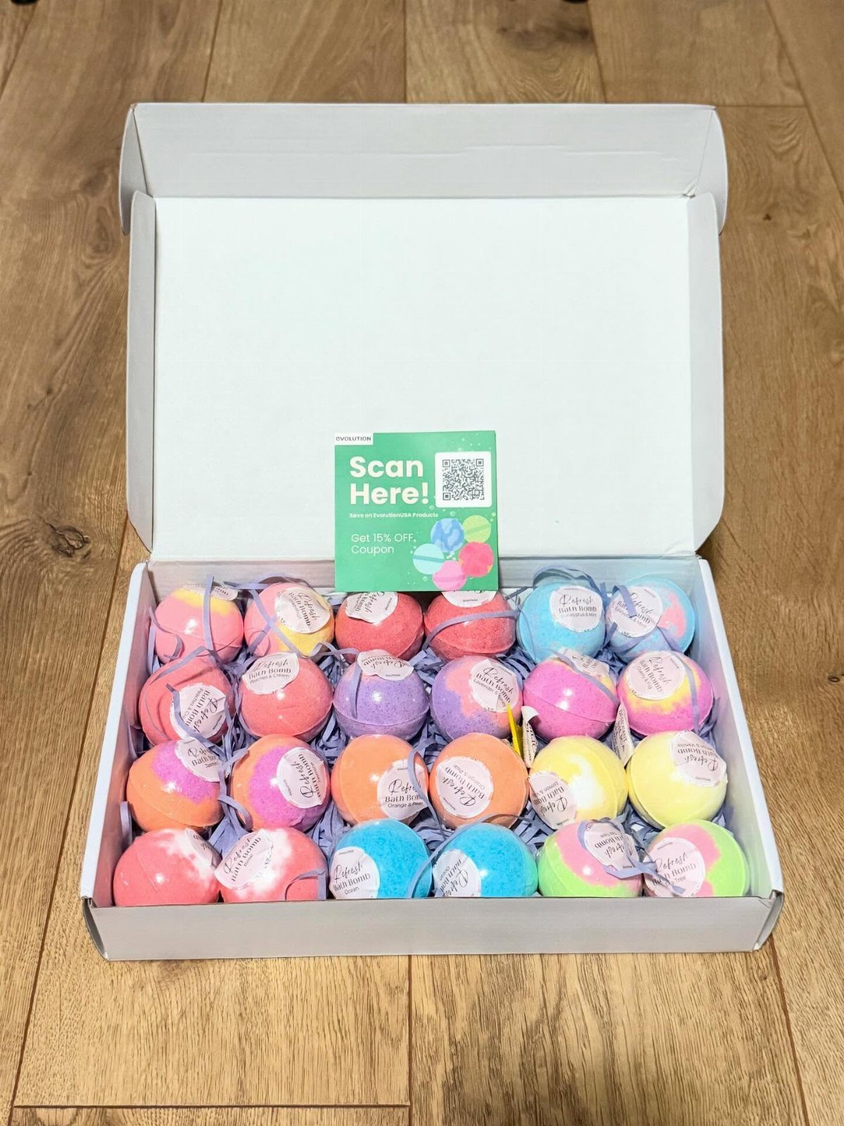 Colorful bath bombs in a white gift box on a wooden floor.