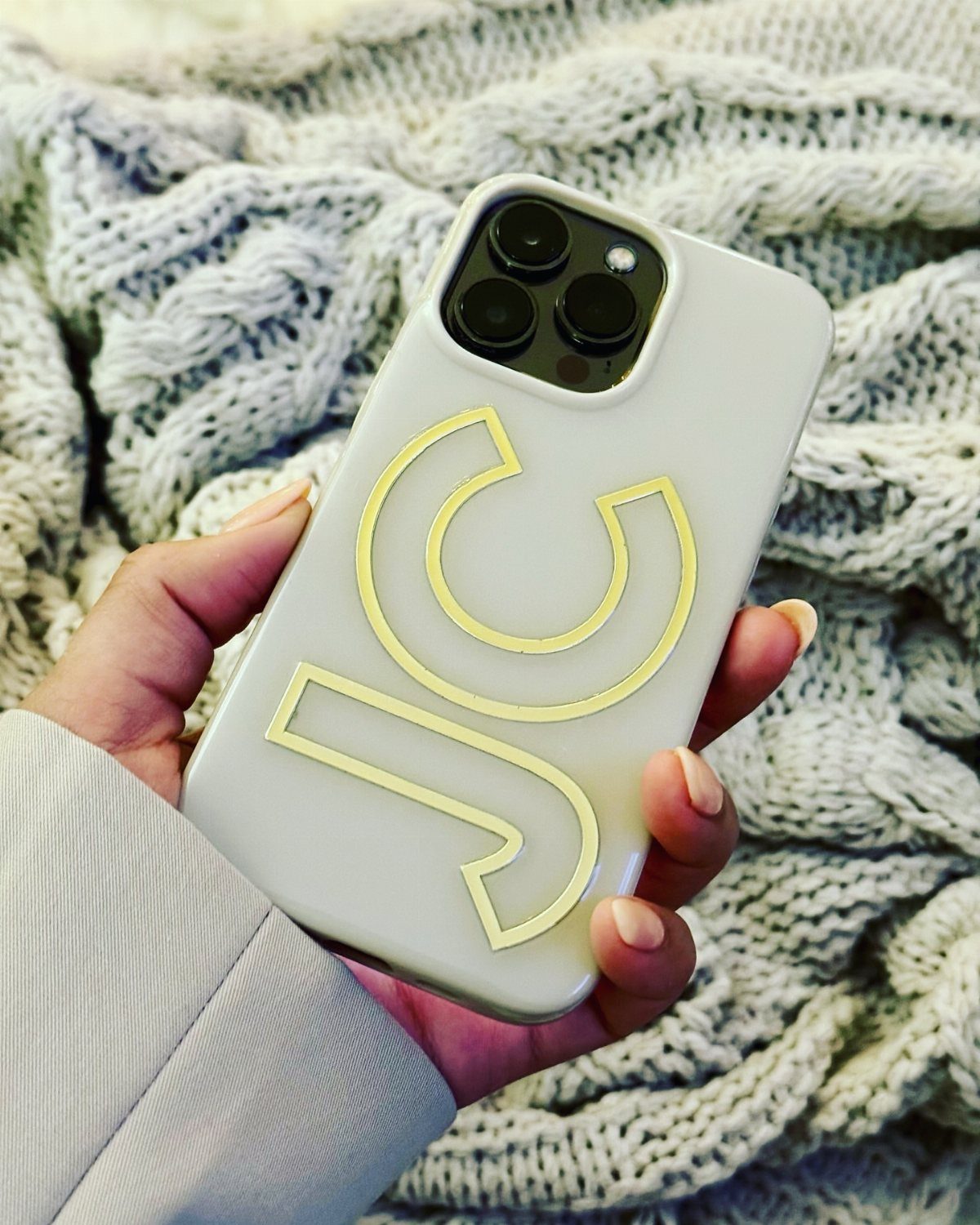 White phone case with pale yellow initials JC held against a grey knit blanket