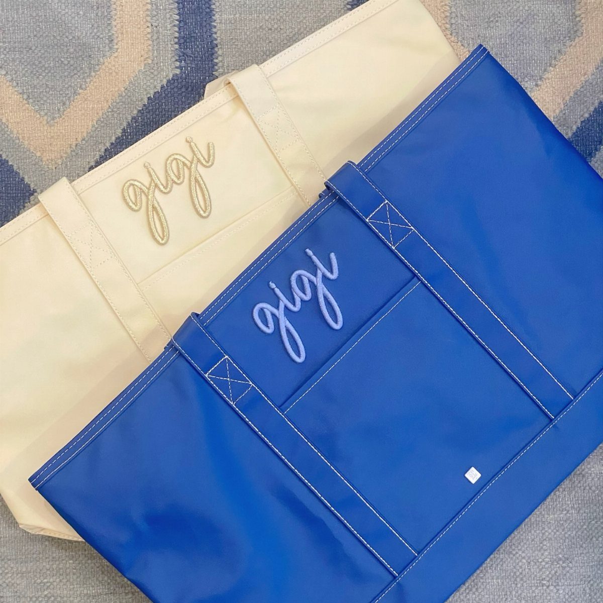 Two personalized tote bags in cream and blue with cursive name embroidery.