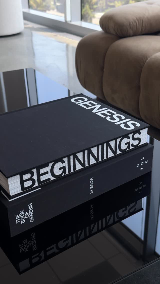 Two black hardcover books titled Genesis and Beginnings on a reflective black table.