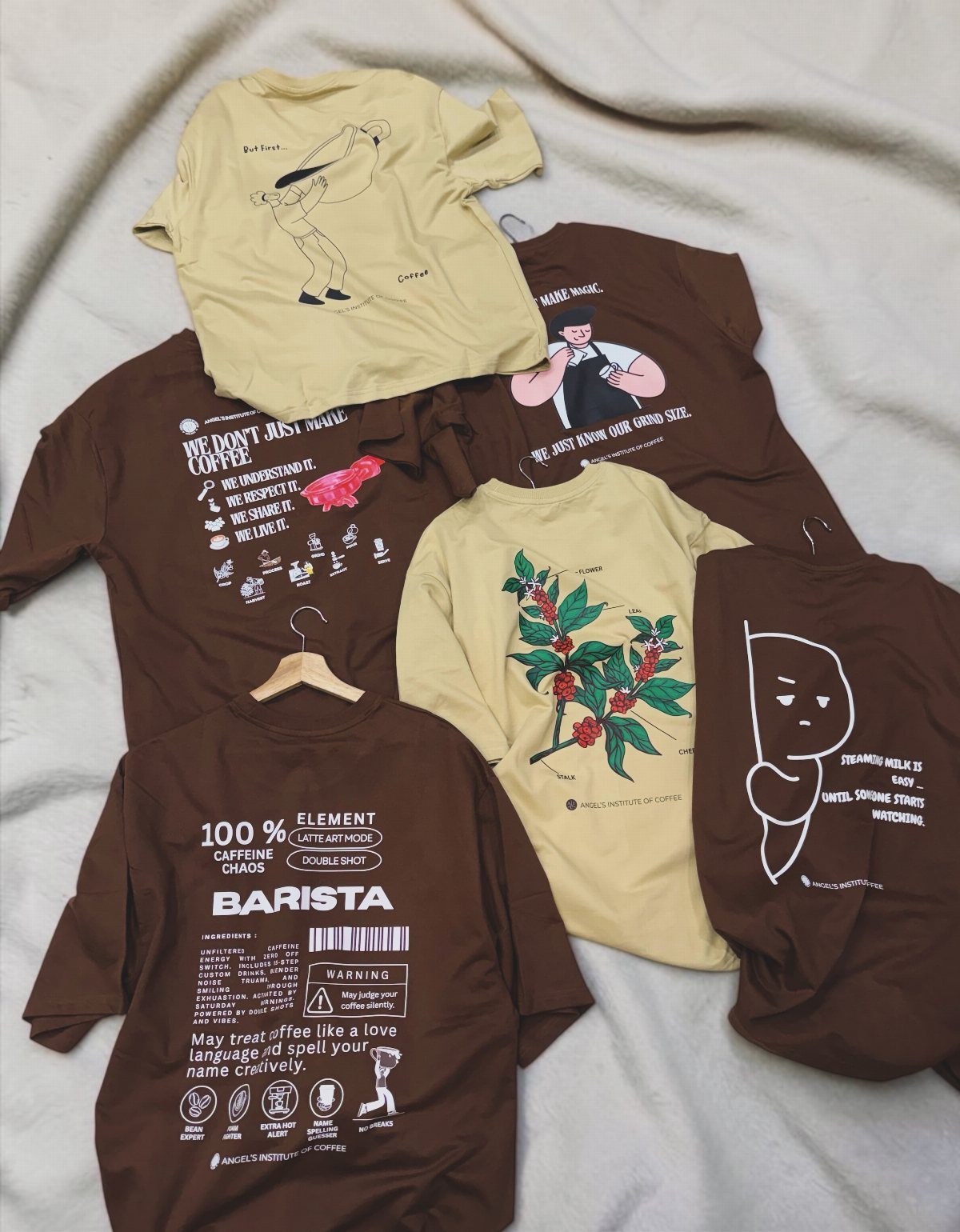 19 Coffee Fan Gifts for Every Budget and Brew Style 5 Coffee-themed graphic t-shirts in brown and beige colors laid on a grey cloth.