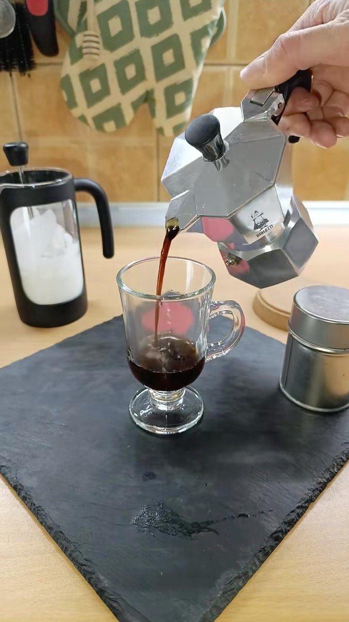 19 Coffee Fan Gifts for Every Budget and Brew Style 7 Silver Moka pot pouring dark coffee into a small clear glass cup.