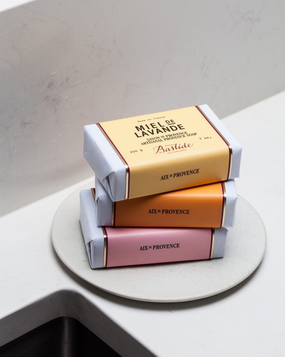 Three stacked bars of Bastide soap in colorful wrappers on a marble tray.