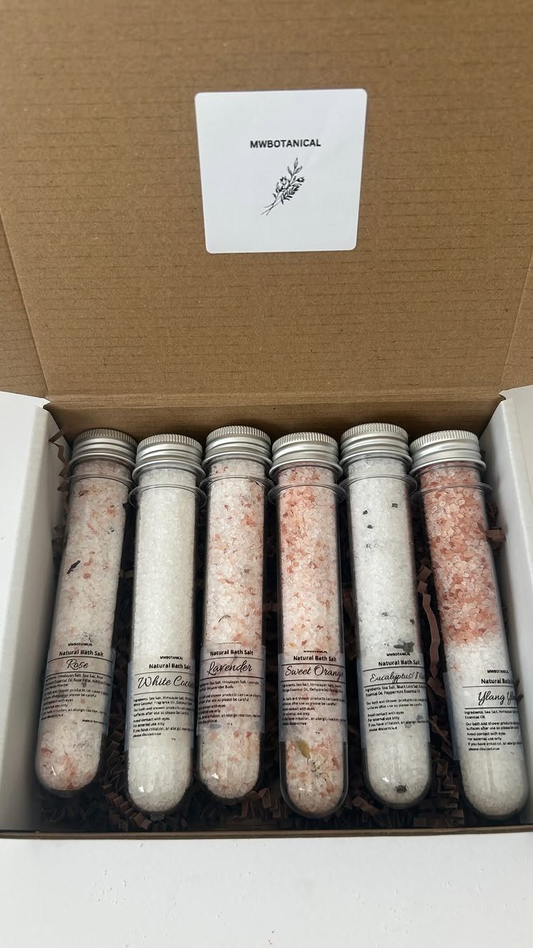 Six glass tubes filled with colorful bath salts inside a brown cardboard gift box.