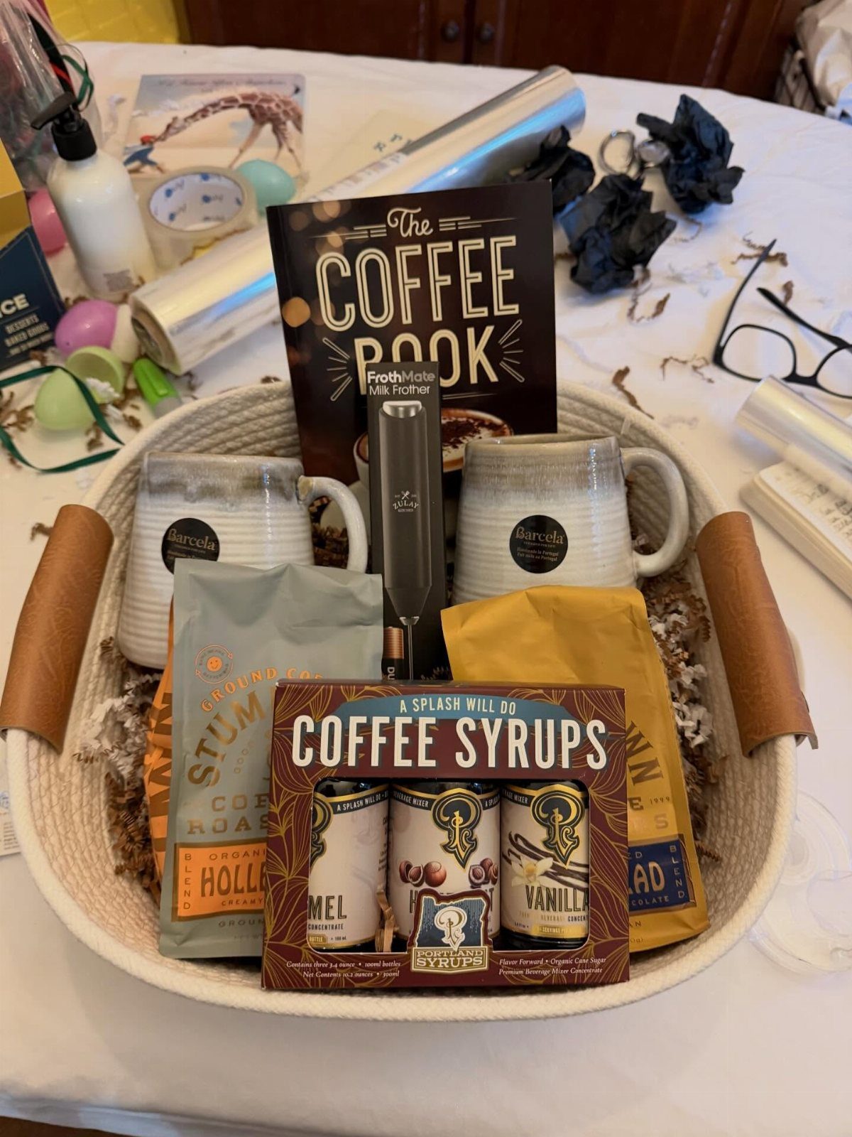 Coffee gift basket with mugs, coffee beans, syrups, and a coffee book.