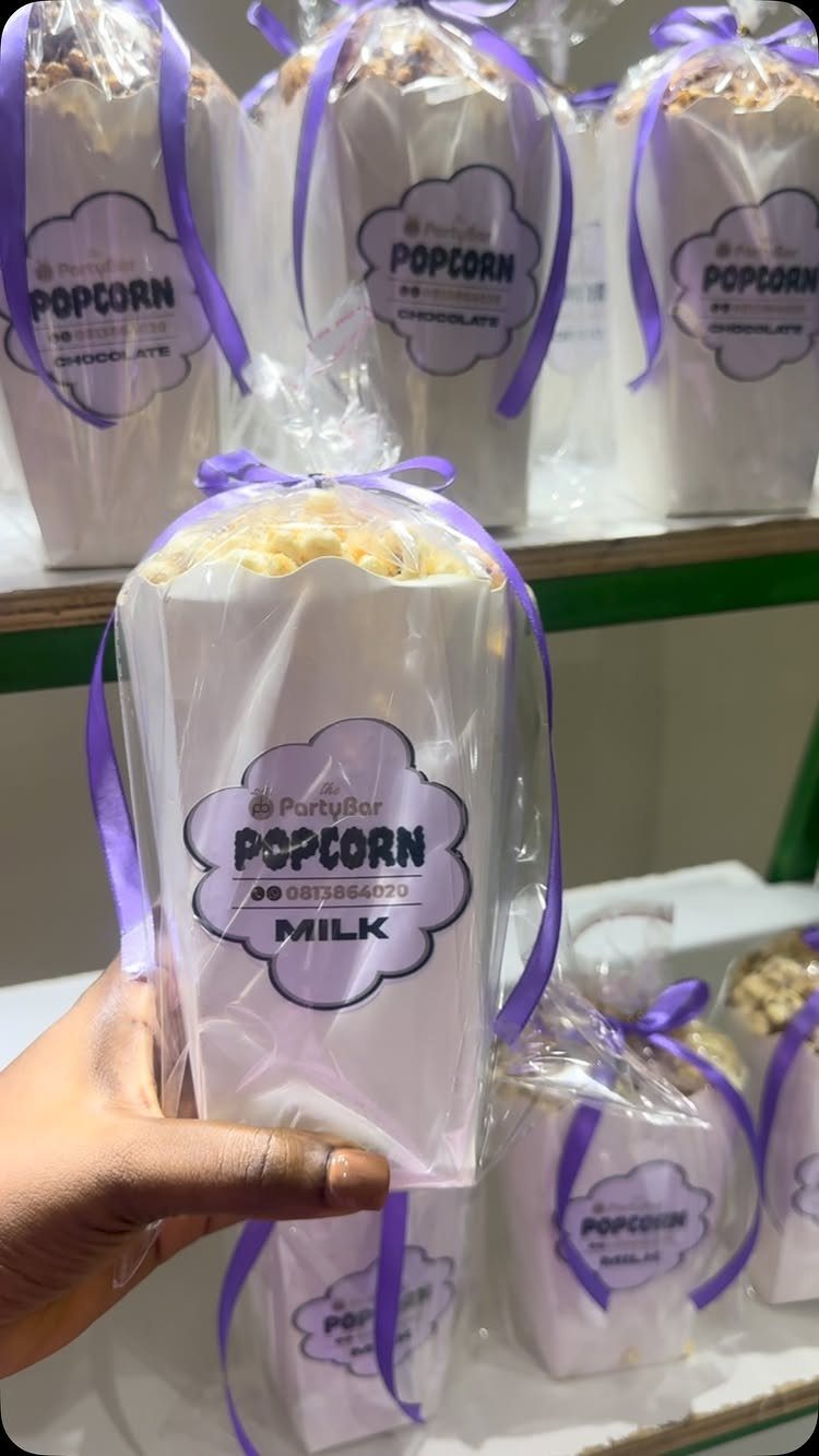 Popcorn in white cones wrapped in clear plastic with purple ribbons and labels.