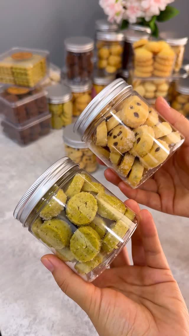Hands holding clear jars filled with chocolate chip and green homemade cookies.