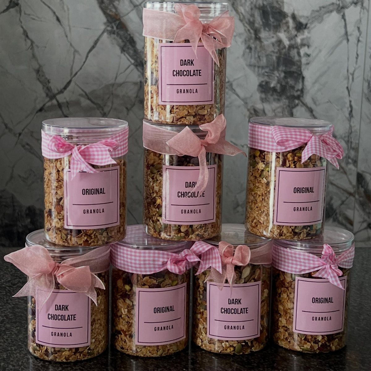 Clear plastic jars of homemade granola with pink labels and gingham ribbons.